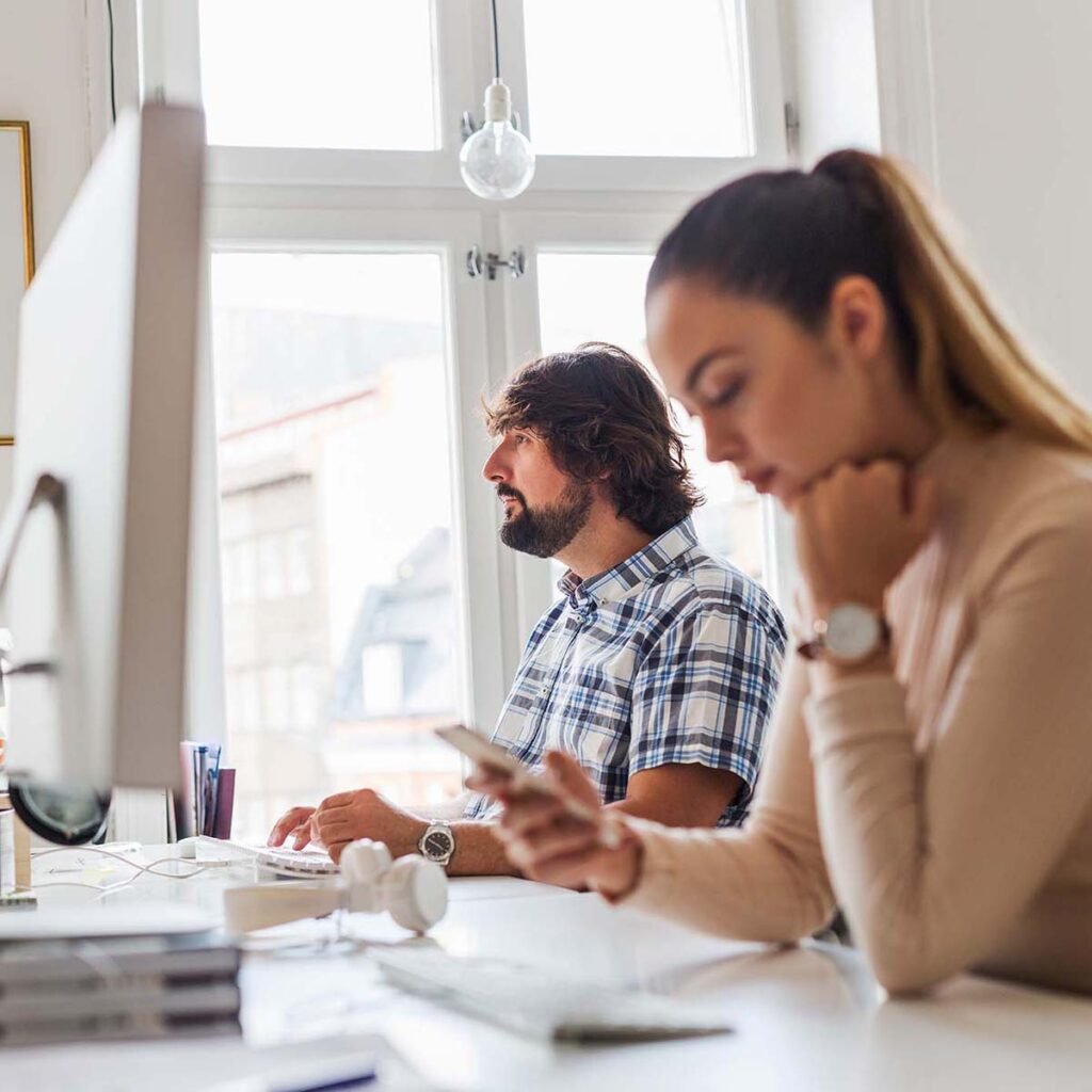 Two focused individuals working at desks in a bright office environment.