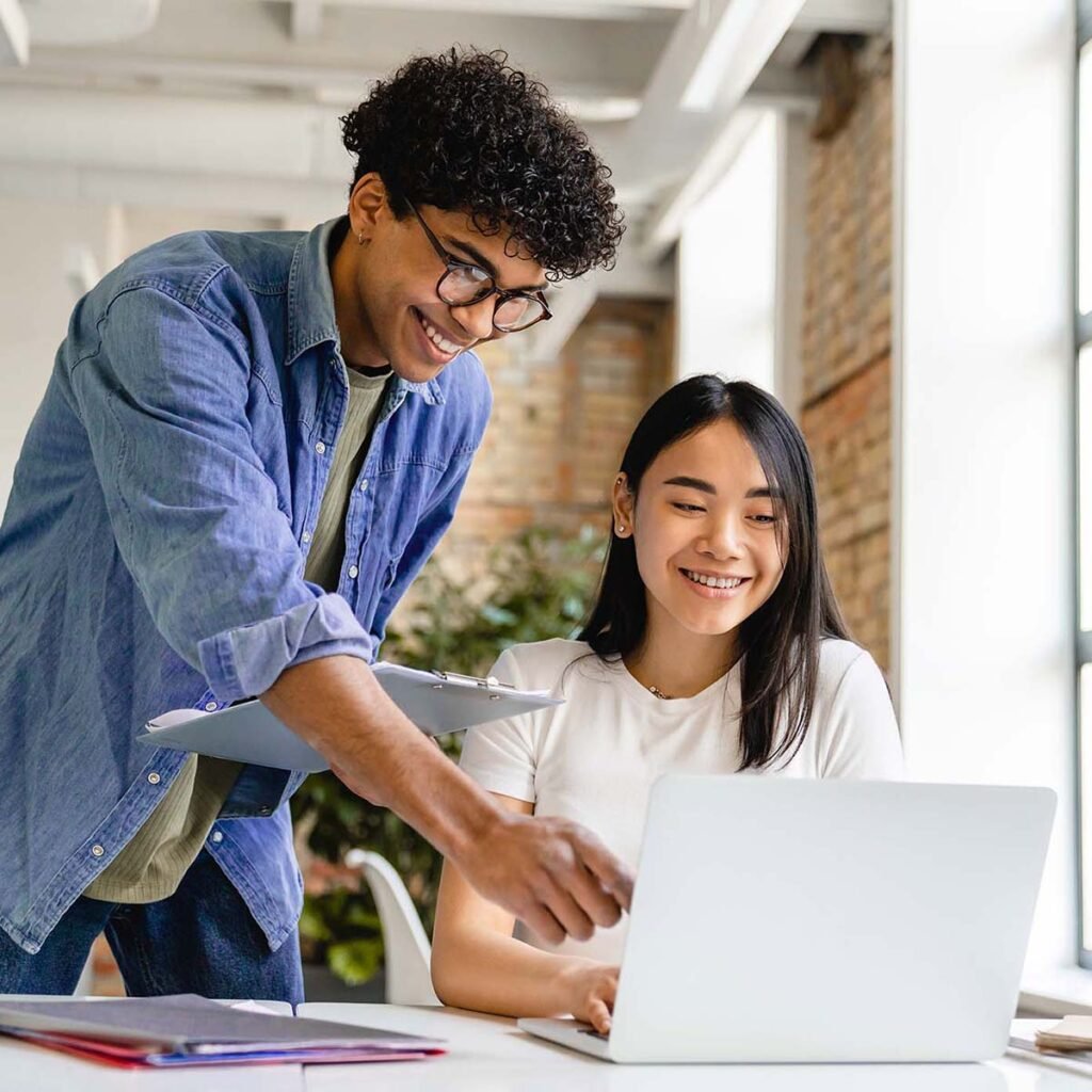 Two young business partners working together on a laptop in a modern office.